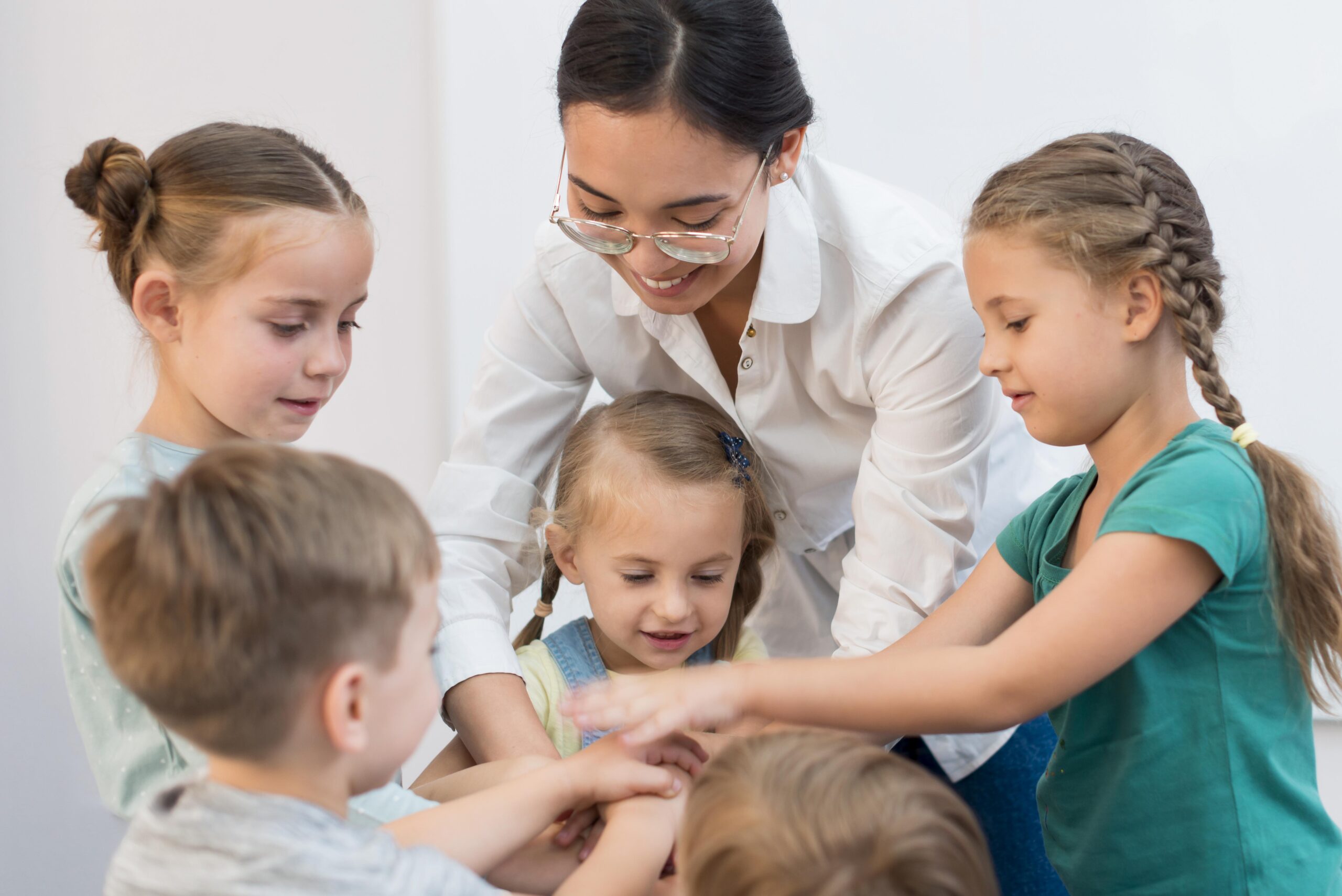 "Enseignante souriante mettant ses mains en cercle avec un groupe d'enfants jouant à un jeu."